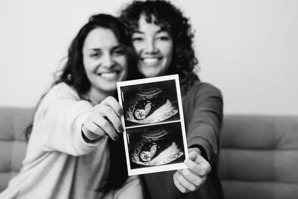 LGBT lesbian couple holding ultrasound scan of growing baby in pregnancy time - Focus on photo